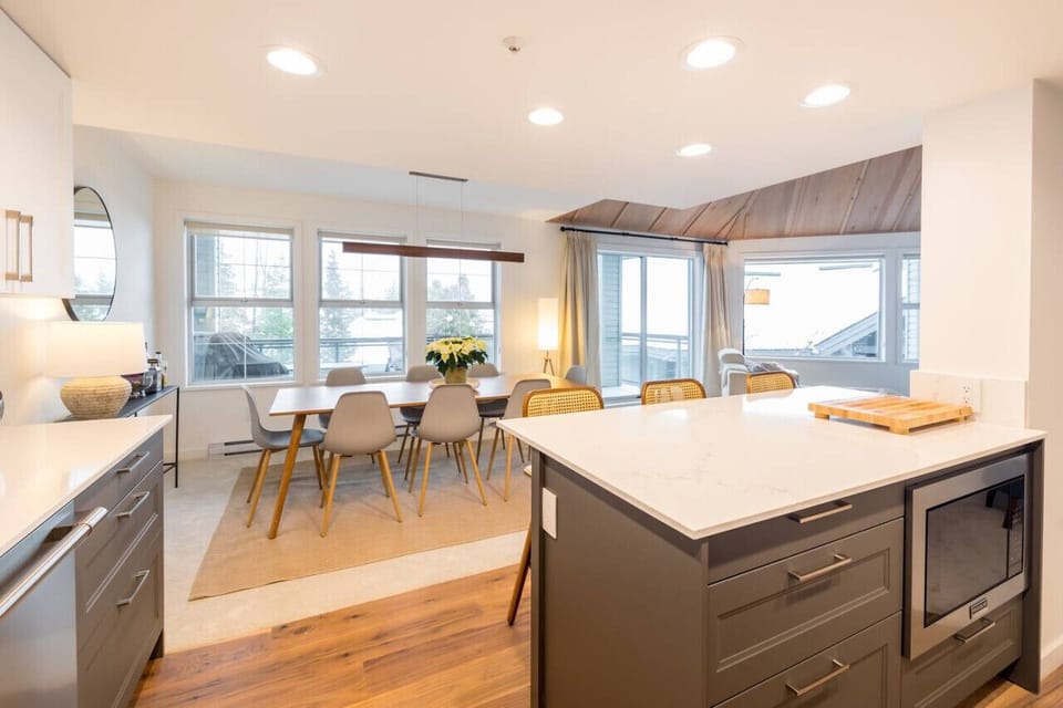 The dining area, bathed in sunlight streaming through expansive windows, offers a view of the balcony from the kitchen. A perfect blend of indoor elegance and outdoor charm!