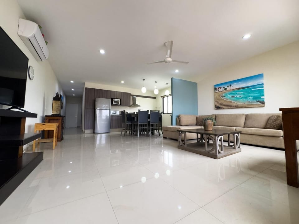Living area features a tan sectional sofa, wood coffee table, blue accent wall, and open kitchen with gray cabinetry.