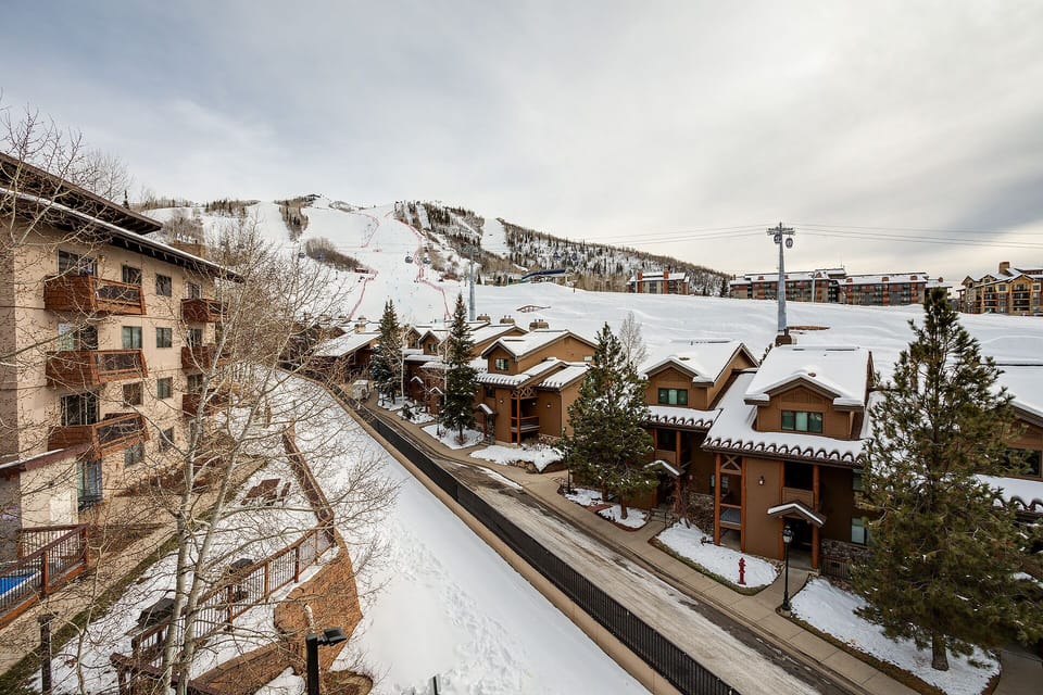 Elevated mountain resort village with ski slopes, chairlifts, and snow-covered residential buildings nestled in a winter landscape.
