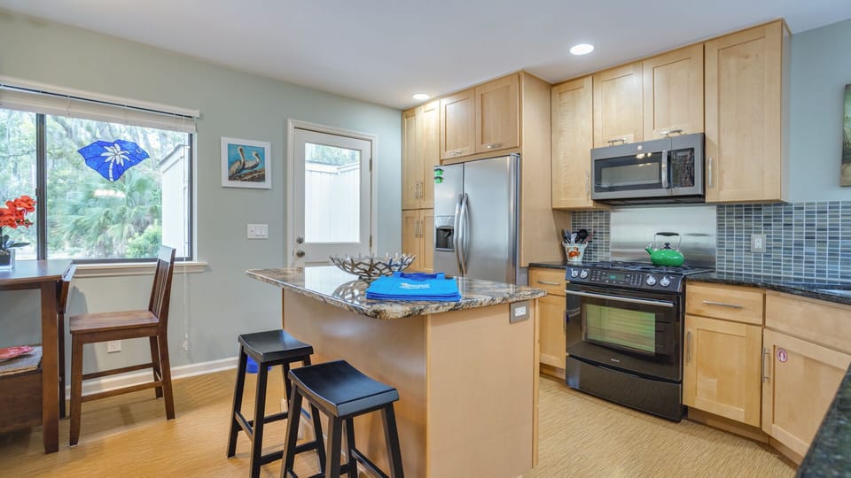 This bright, well-appointed kitchen features warm wood cabinetry, granite countertops, and a stylish tile backsplash.