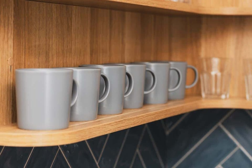 A corner shelf with gray mugs and glasses neatly arranged, adding a functional and decorative element to the kitchen.

