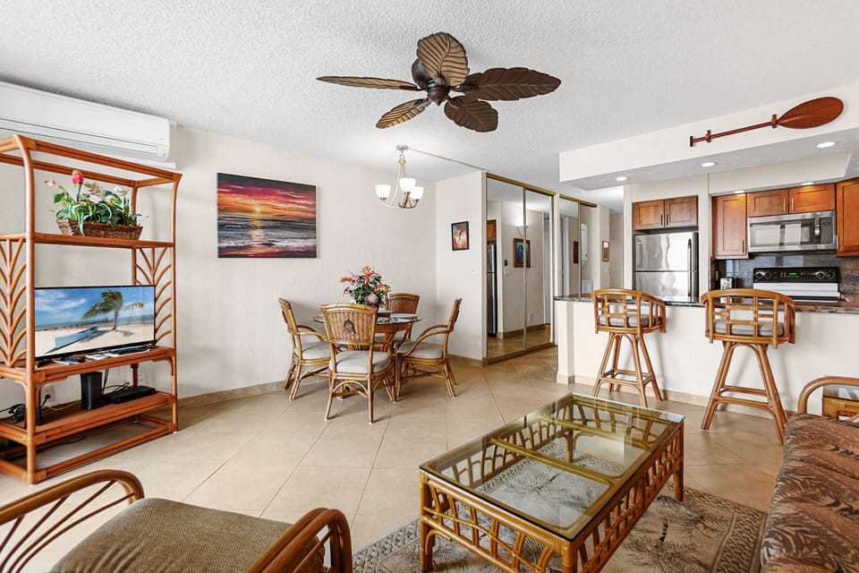 An inviting tropical-themed living space with rattan decor and a glass dining table, overlooking a serene outdoor view. A blend of relaxation and functionality.