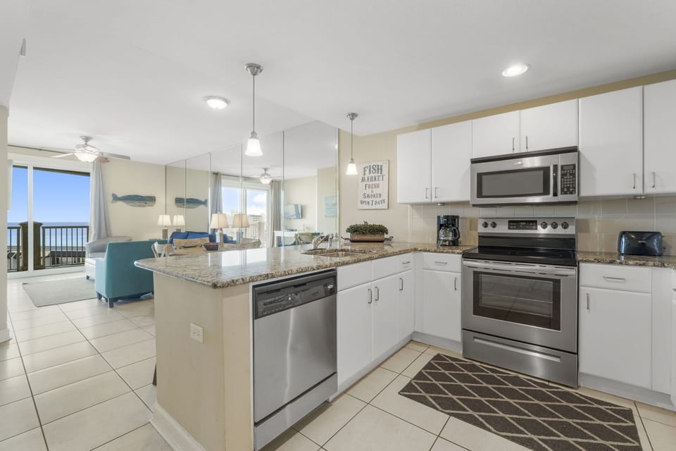 Modern kitchen with stainless steel appliances and granite countertops overlooking the living area and ocean view.