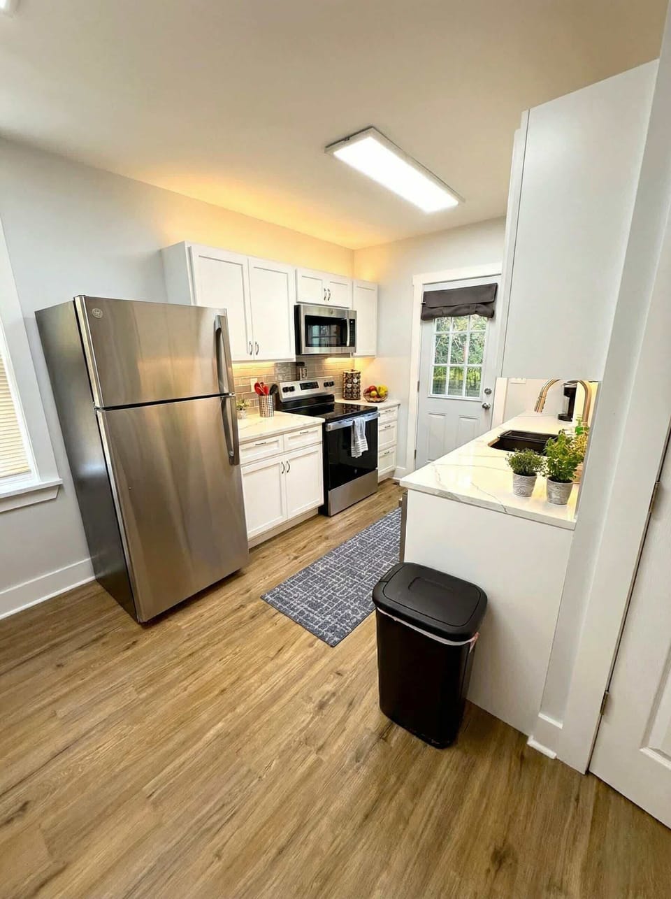 Galley kitchen with stainless steel appliances, white cabinetry, and natural light.