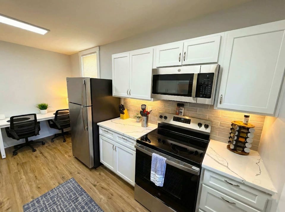 Kitchen with stainless steel refrigerator, stove, microwave, white cabinetry, and workspace nook.