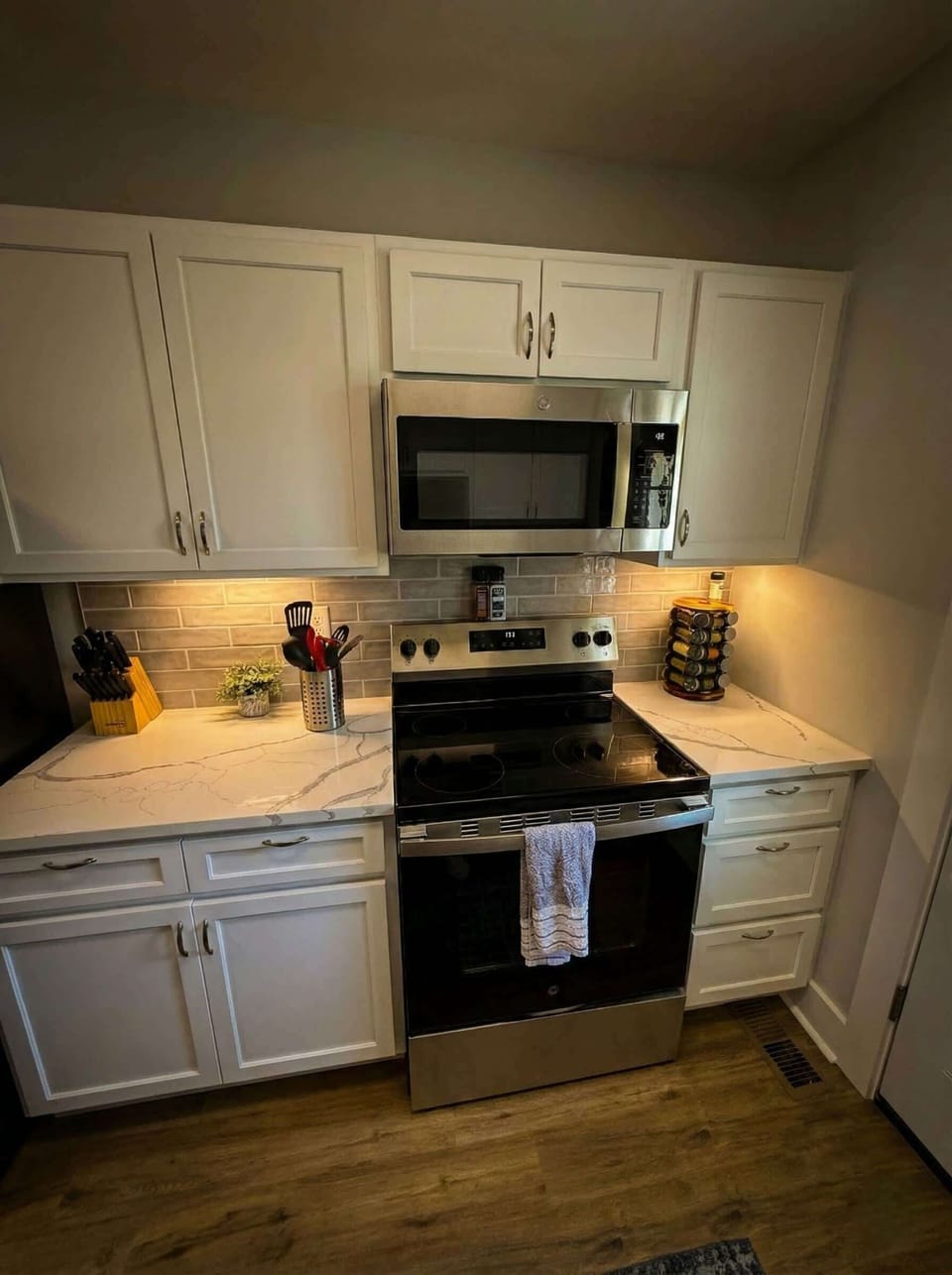 Kitchen cooking area with stainless steel stove, microwave, and white cabinetry.