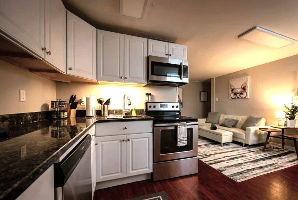 Kitchen and living area with stainless steel appliances, white cabinetry, sofa, and TV.