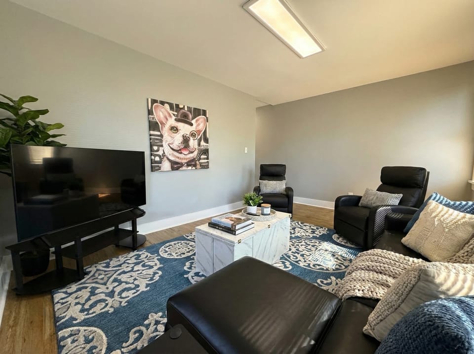 Living room with TV, recliner seating, sofa, coffee table, and large area rug.