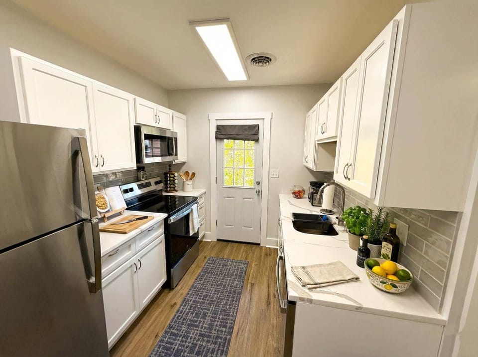 Galley kitchen with stainless steel appliances, white cabinetry, and tile backsplash.