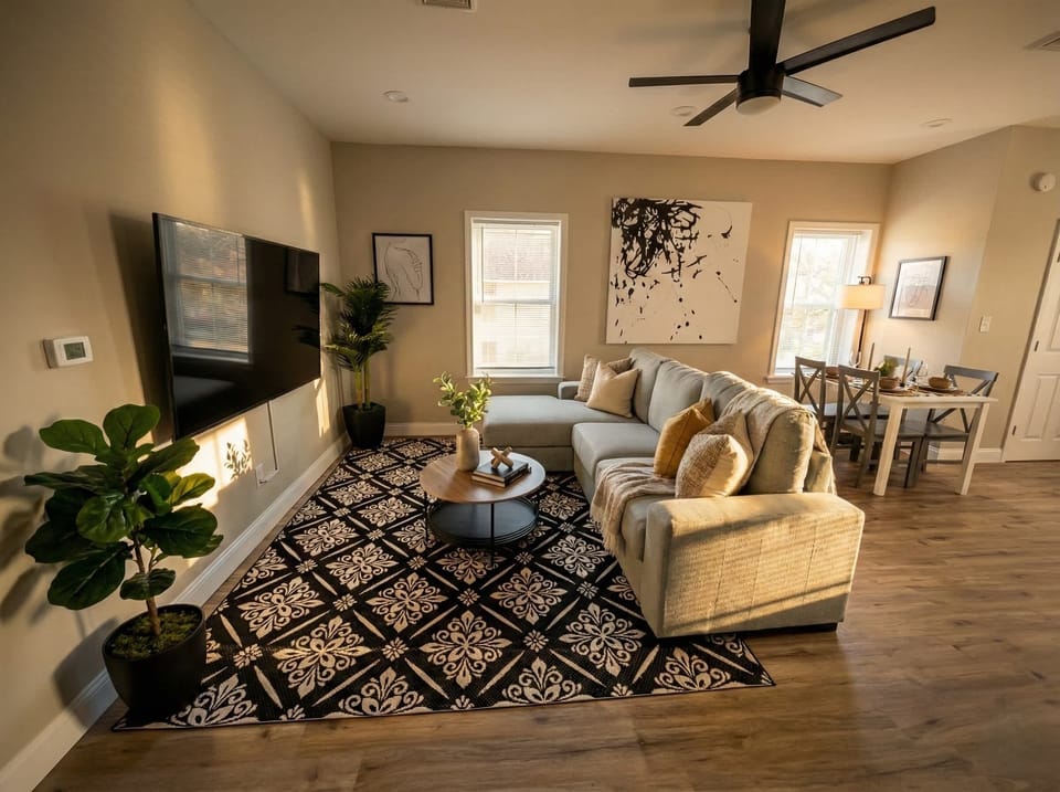 Living room with sofa seating, wall-mounted TV, ceiling fan, and dining area nearby.
