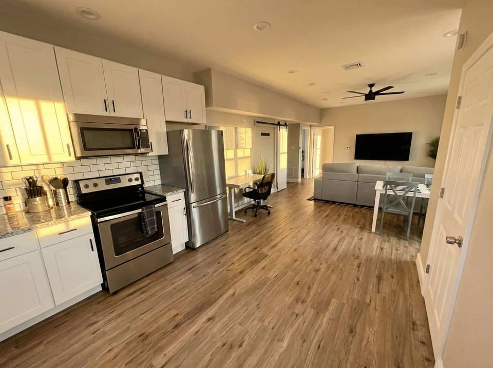 Open kitchen and living area with stainless steel appliances, desk nook, and TV seating.