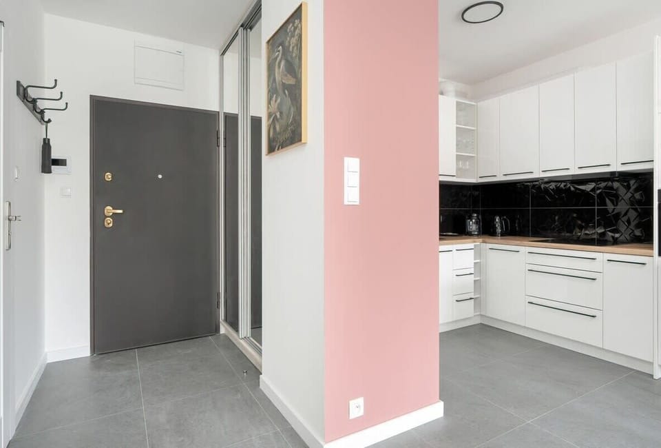 An entryway with light walls and pink accents, leading to a modern kitchen with black and white decor.

