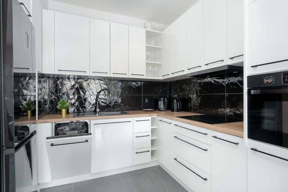 A modern kitchen with white cabinetry and black marble backsplash, combining style and functionality.

