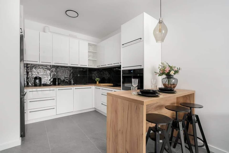 A contemporary kitchen with sleek white cabinets, black accents, and a wooden dining island, providing a functional and elegant space.
