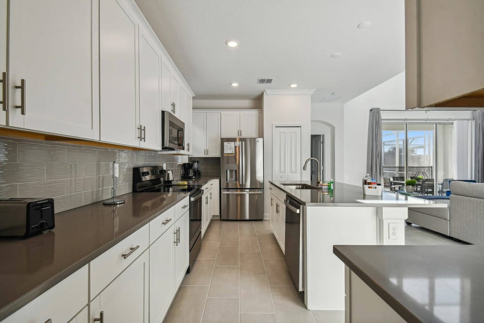 This bright kitchen combines sleek white cabinetry with a rich dark countertop for a stylish look. Natural light floods in through the large window, highlighting modern appliances that await your culinary creations.