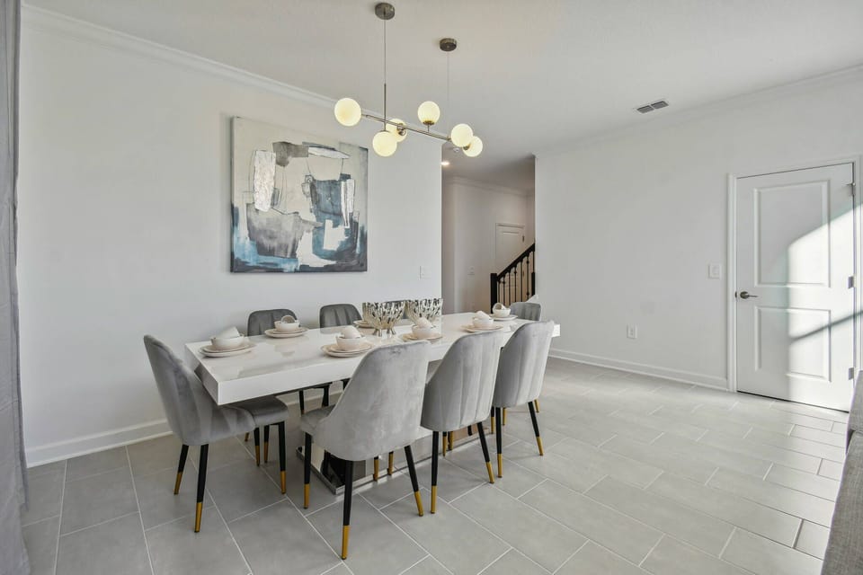 Welcome to a stylish dining area featuring a spacious table and soft gray upholstered chairs, perfect for gatherings. Contemporary lighting and abstract artwork create an inviting atmosphere for memorable shared meals.