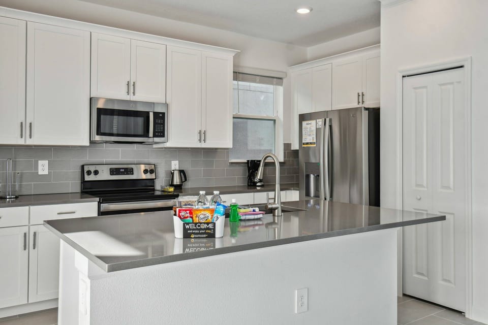 Step into a bright, well-appointed kitchen featuring sleek, white cabinetry and a spacious island topped with elegant gray stone. Modern appliances and ample natural light create a wonderful atmosphere for culinary adventures.