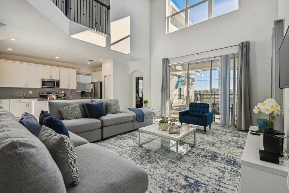 Unwind in the spacious living area featuring a plush gray sectional and vibrant blue accents, ideal after your adventures. Large windows fill the room with natural light, enhanced by elegant drapes for a touch of sophistication.