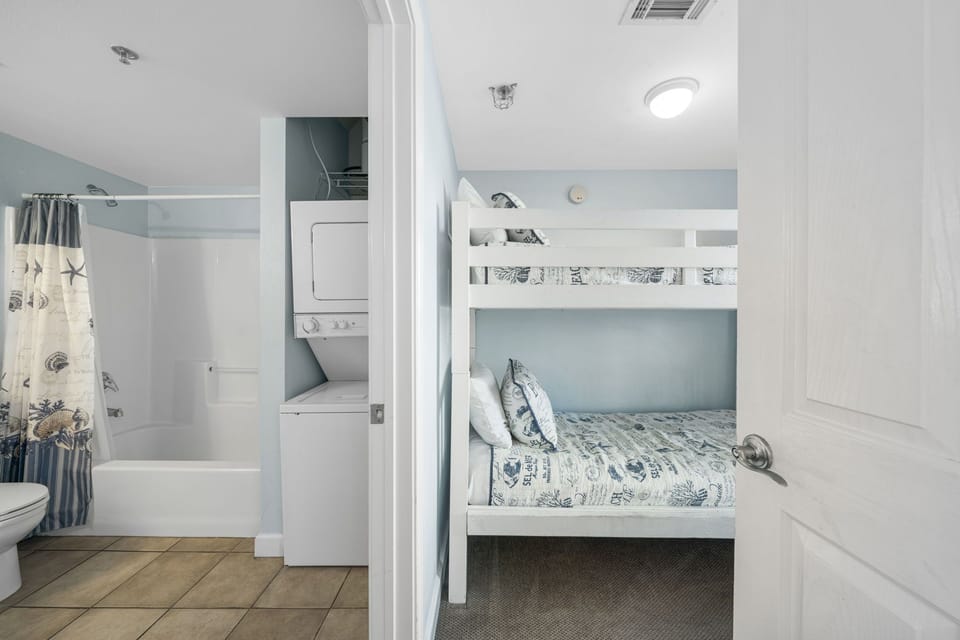 Compact bedroom with bunk beds adjacent to a bathroom featuring a stacked washer and dryer.