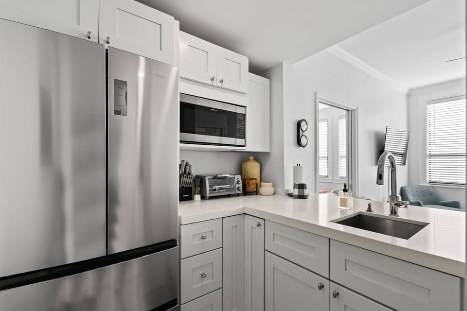 Kitchenette with a Toaster oven, microwave, fridge, Keurig coffee maker, glasses, plates, and cutlery.
