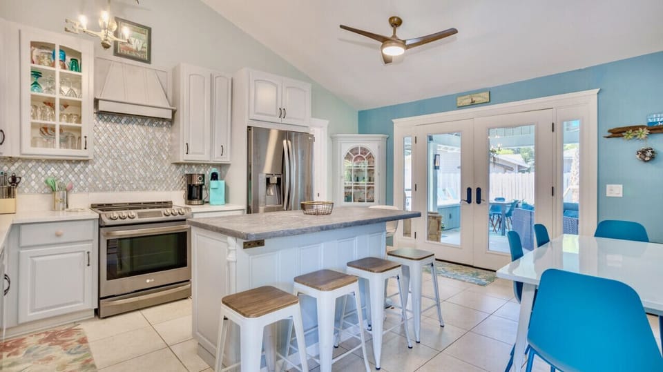 Inside dining options include a modern white table with four ocean teal chairs and four stools at the kitchen island. The double doors lead to other dining areas.