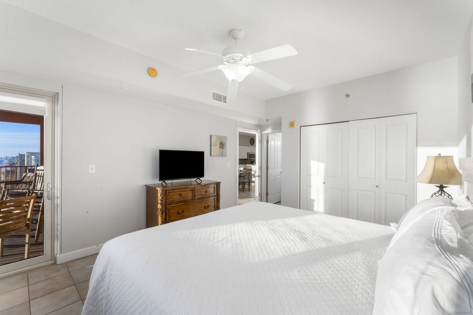 Bright bedroom with white walls and a wooden dresser featuring a flat-screen television.