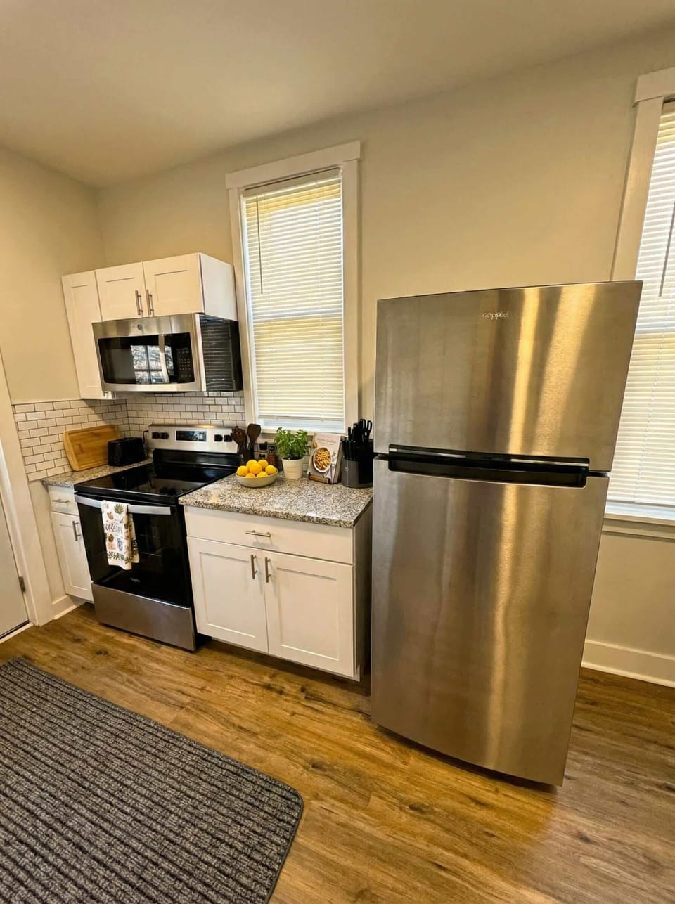 Compact kitchen with stainless steel refrigerator, stove, microwave, and white cabinetry.
