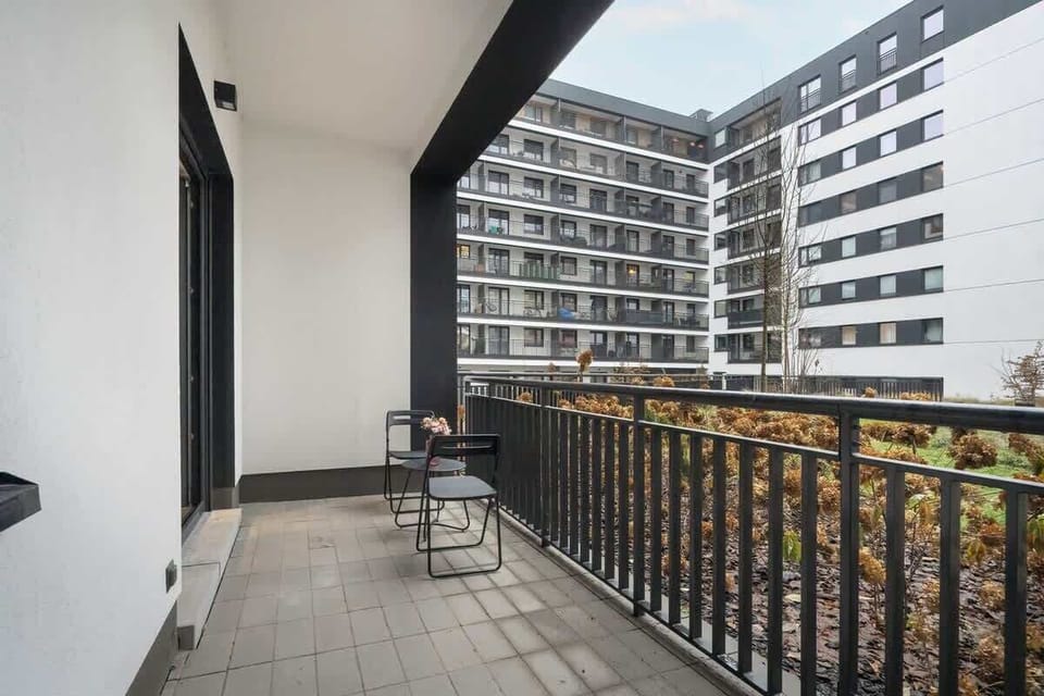 A spacious balcony with black railings overlooking a courtyard surrounded by modern apartment buildings.
