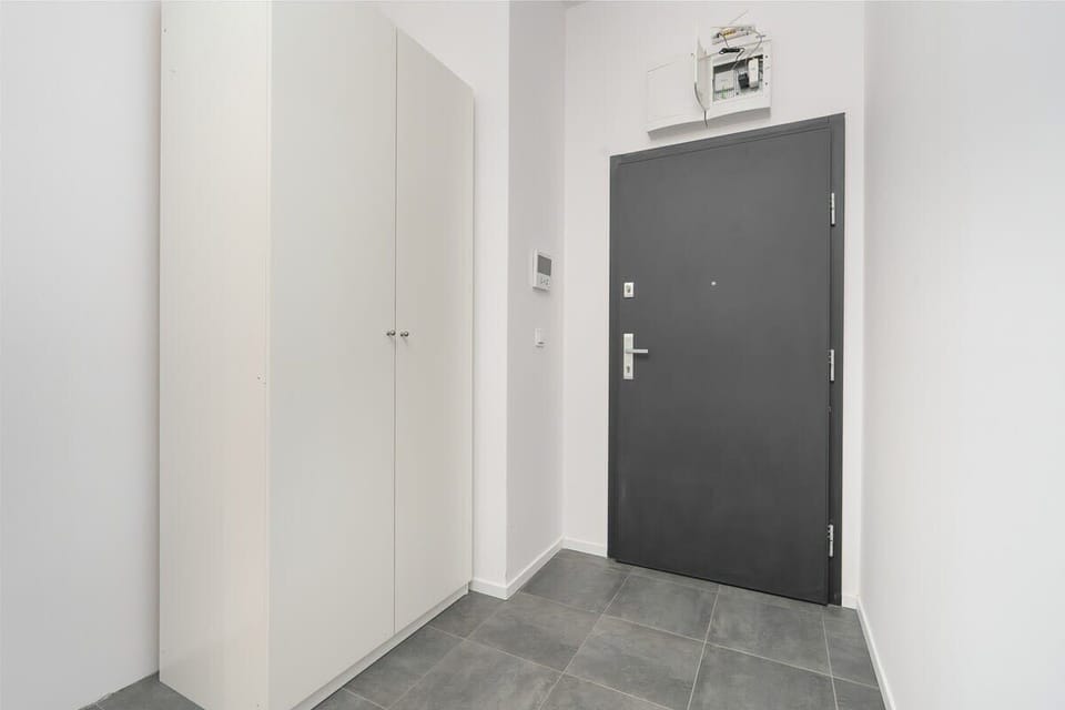 An entryway with grey floor tiles, a secure door, and minimalist hallway design.
