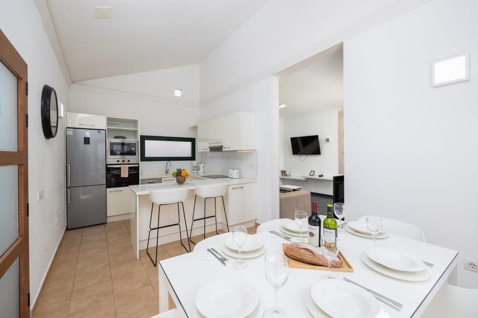 Open-plan living room with sofa, dining area, kitchen, ornamental fireplace, A/C, WiFi internet, and satellite TV