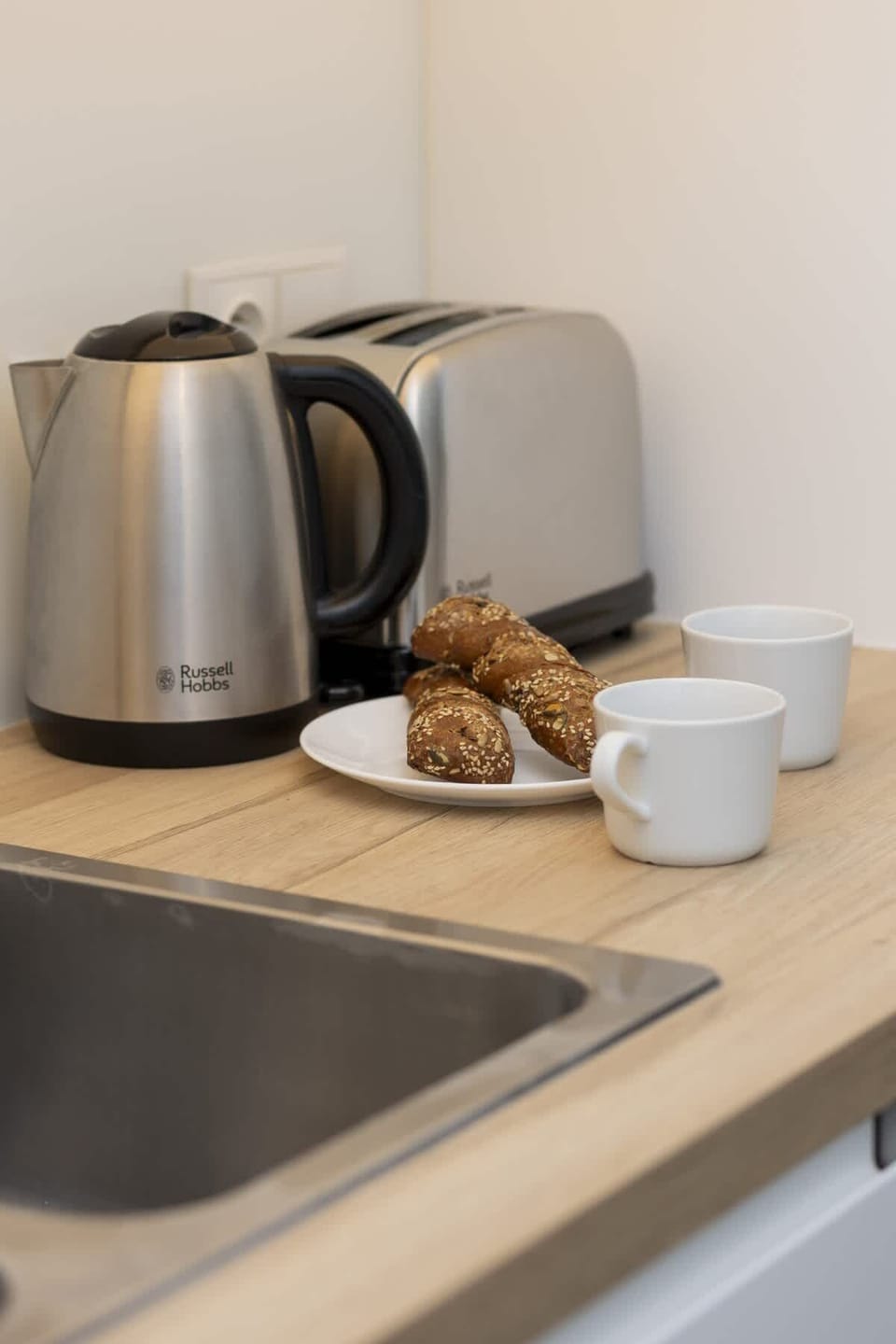 A compact kitchen corner with a kettle, white cup, and a modern countertop, providing convenience and style.
