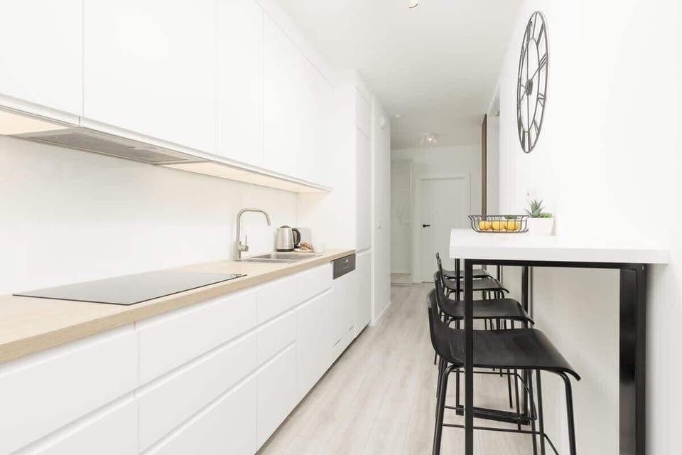 A modern kitchen with white cabinets, integrated appliances, and a breakfast bar with high chairs, offering a functional and stylish layout.

