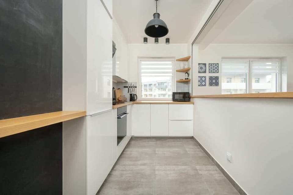 A narrow kitchen with white cabinets, wooden countertops, and modern appliances, offering a clean and functional space.
