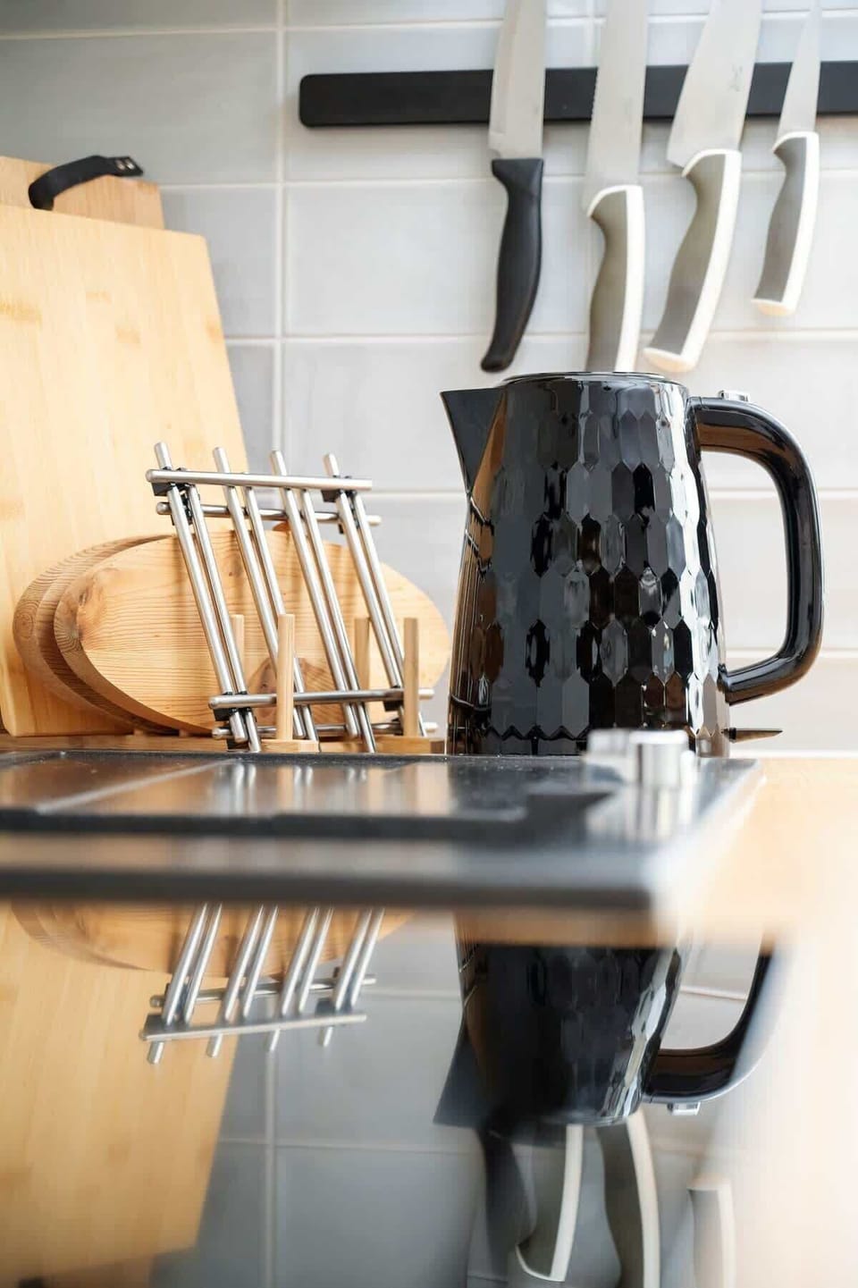 A kitchen corner with a set of knives on a wooden block, a modern kettle, and sleek black and white decor.
