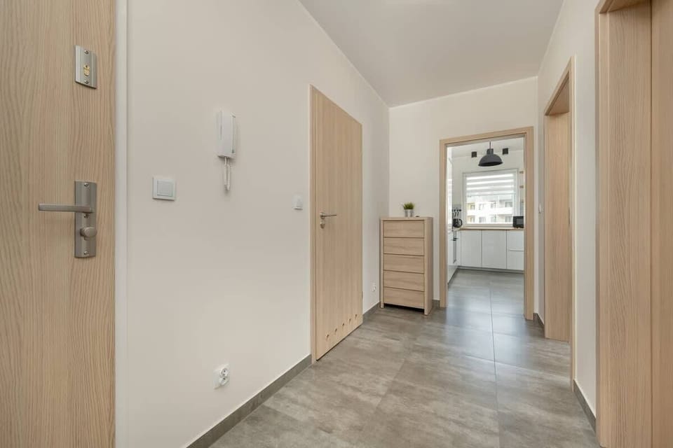 A hallway with wooden doors and light grey floor tiles, leading to different rooms within the apartment.

