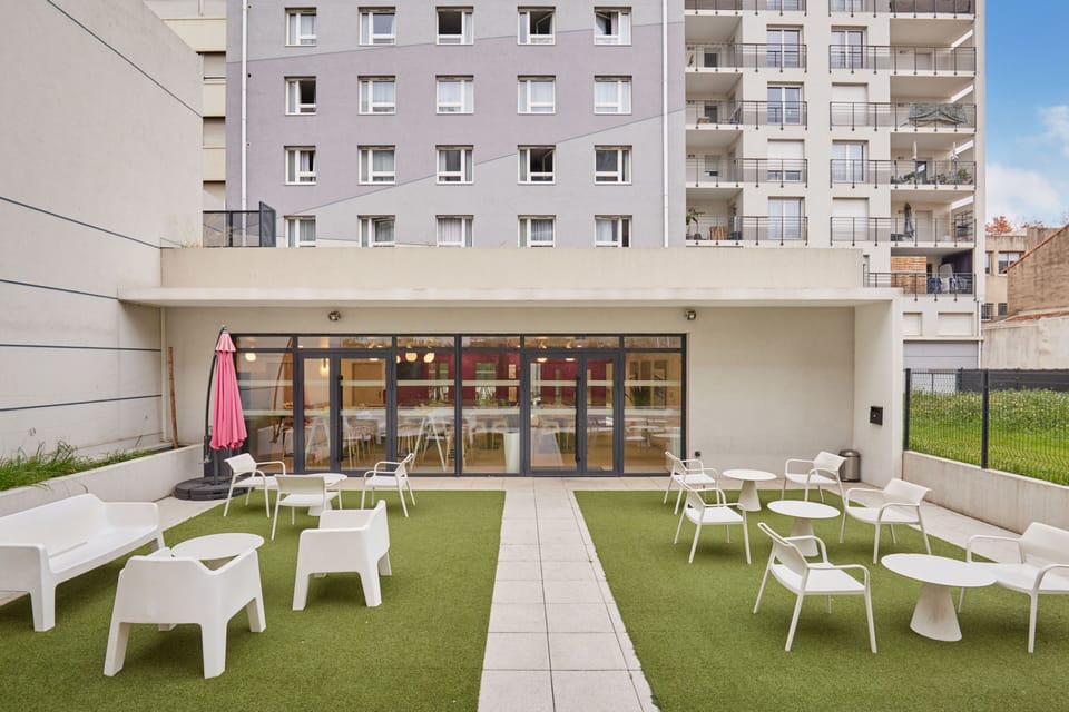 Inviting outdoor seating area with sleek white furniture and a bright pink parasol creating a serene urban oasis.