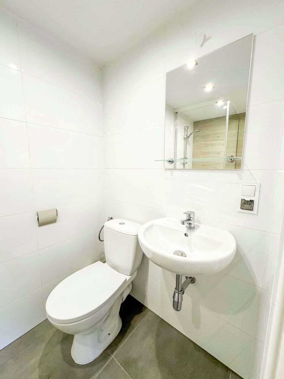 A minimalist bathroom with a white sink, toilet, and light grey tiles, maintaining a clean and functional design.
