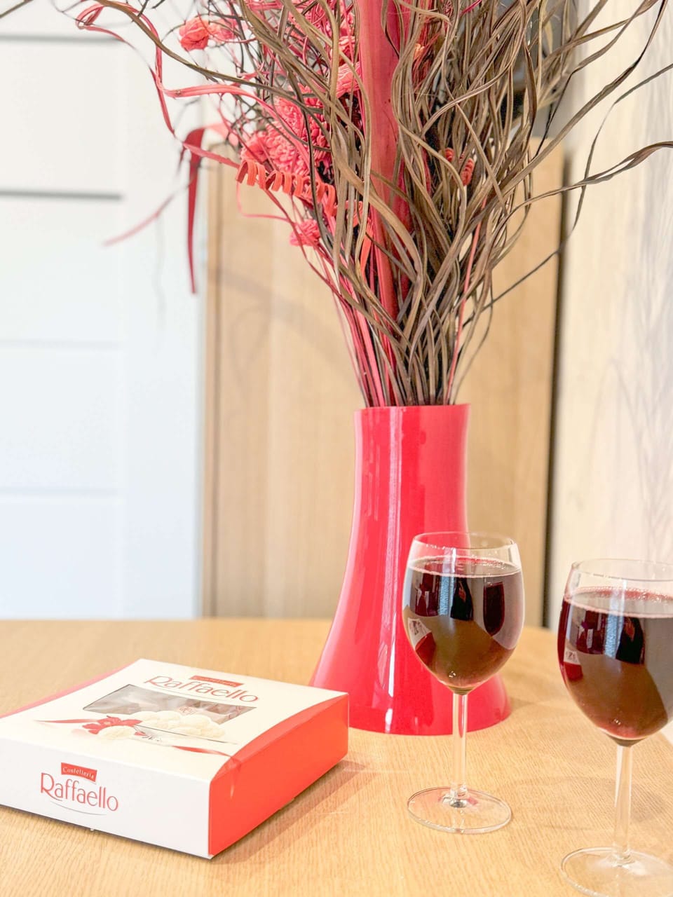 A festive table setting with red branches, wine glasses, and holiday decor, creating a warm and celebratory dining experience.
