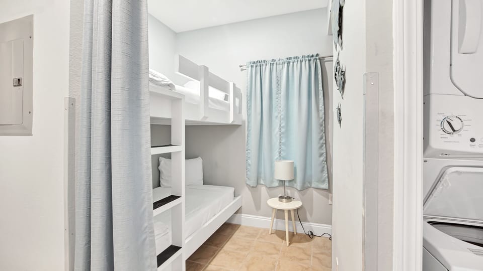 Compact bedroom featuring white bunk beds and soft natural lighting for a cozy stay.