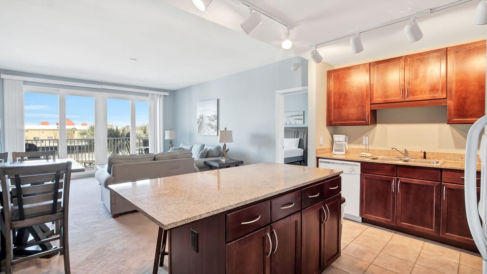 Modern kitchen island with granite countertop overlooking a bright living area and balcony.