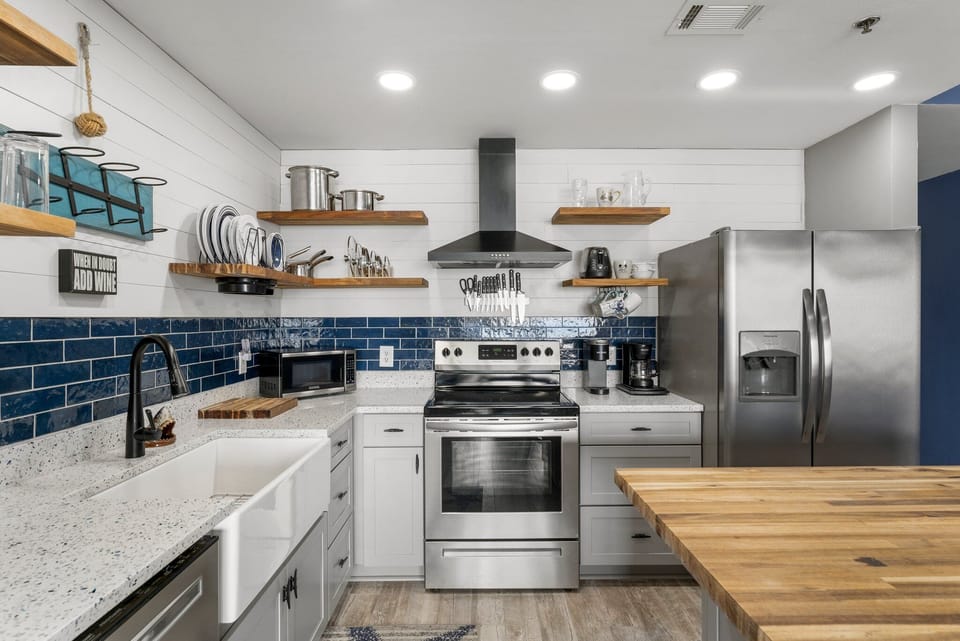 Modern kitchen featuring stainless steel appliances and a farmhouse sink with blue tile backsplash.