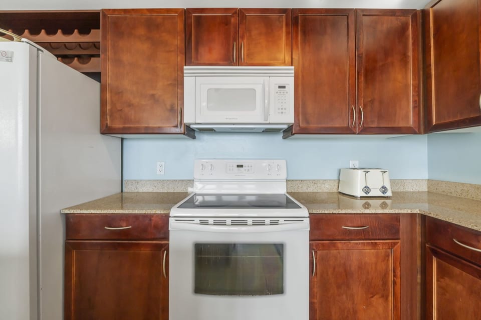 Kitchen area featuring a white electric stove, microwave, and wooden cabinetry.