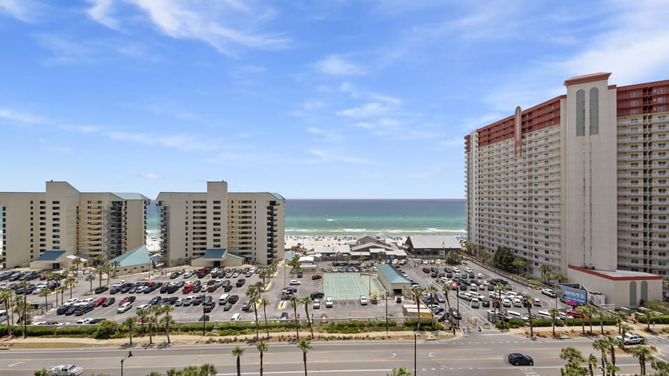 View of the beach and ocean from a high-rise balcony with nearby hotels and a pool area.