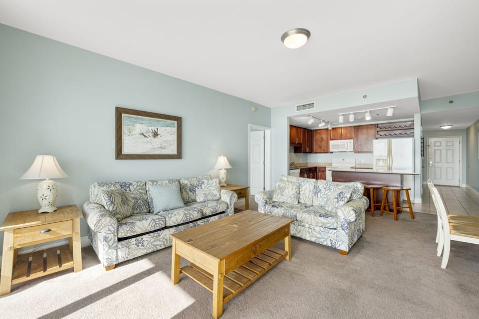Living area with floral sofas and an open kitchen featuring wooden cabinetry