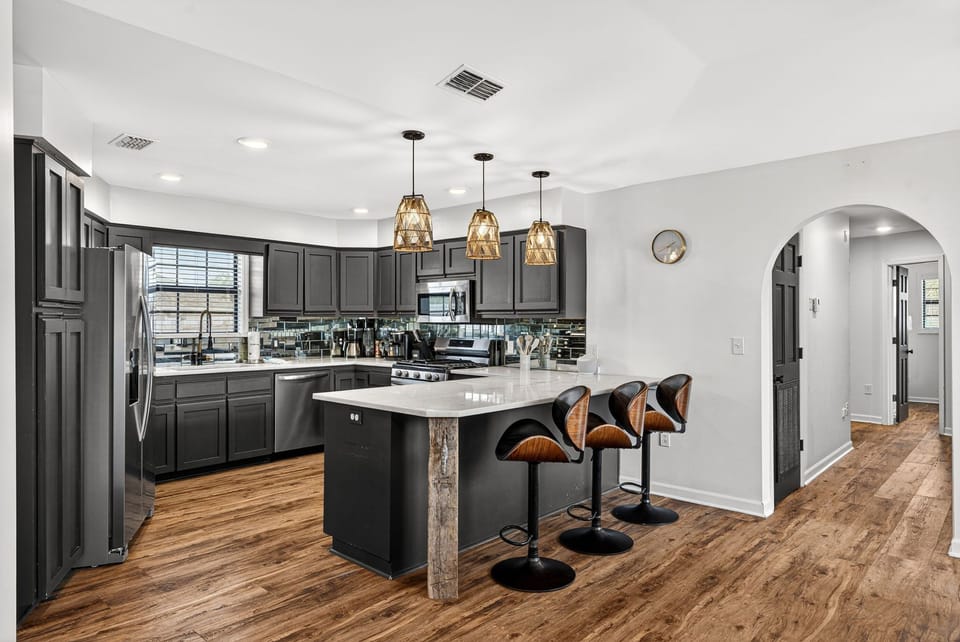 Your stylish kitchen features dark cabinetry, sleek marble countertops, modern pendant lighting, and a spacious island with comfortable seating—perfect for cooking and gathering together.