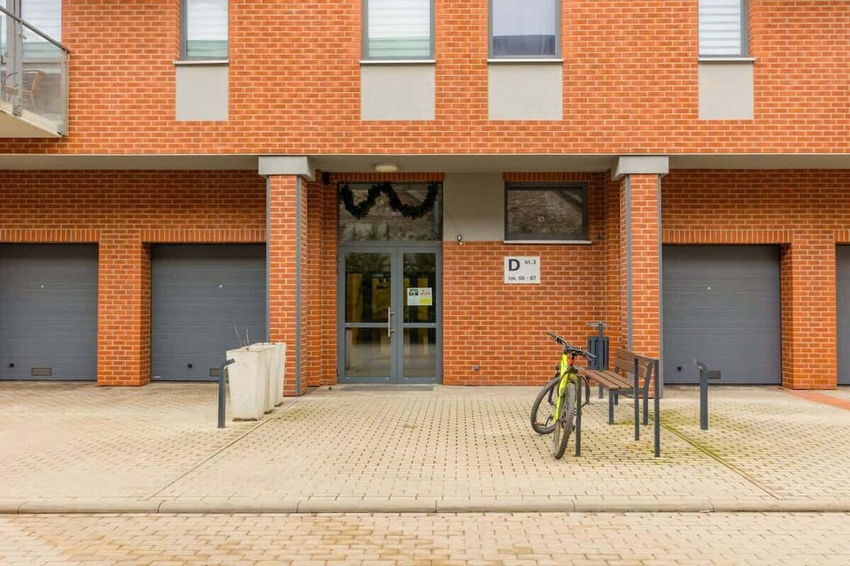 An exterior view of the apartment building with a red-brick facade, ground-floor garages, and a bicycle parking area.
