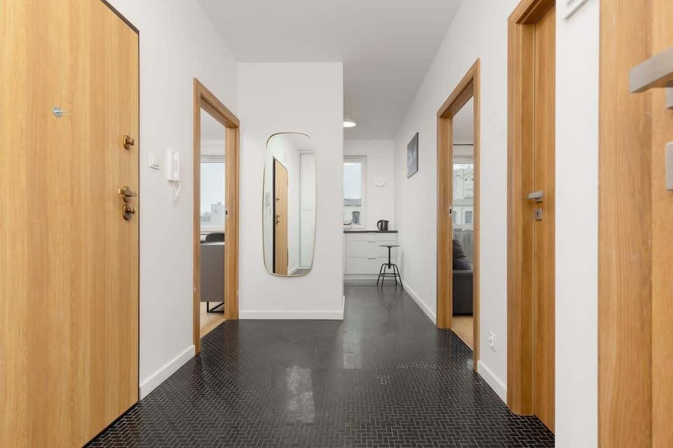 A spacious hallway with wooden doors, black tiled flooring, and a large mirror, enhancing the sense of space and light.
