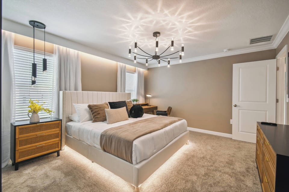 Experience a bright bedroom with a plush king-size bed dressed in soft linens and decorative pillows, alongside a stylish wooden nightstand. The stunning chandelier adds a warm glow, creating a soothing and inviting atmosphere.