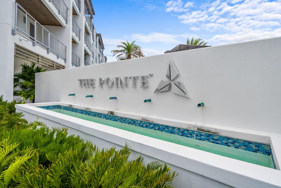 A sophisticated welcome awaits at The Pointe, where modern design meets tropical elegance in this beautifully landscaped entrance.