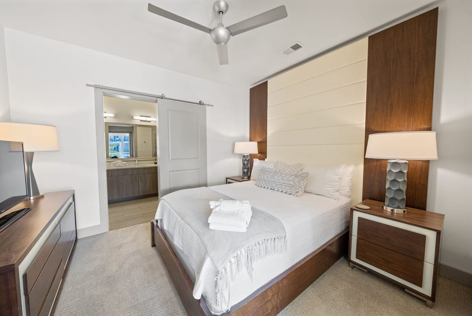 Unwind in your stylish bedroom with plush linens, modern wood accents, and a ceiling fan for perfect comfort.
